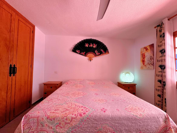 A pink-themed bedroom with a large bed, wooden wardrobe, and two bedside tables on either side of the quilted bedspread.
