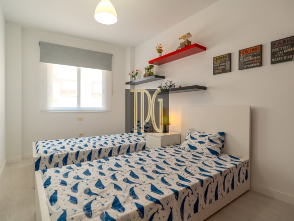 Twin bedroom with two single beds, white headboards, and blue whale-pattern bedding under a window with a roller blind.