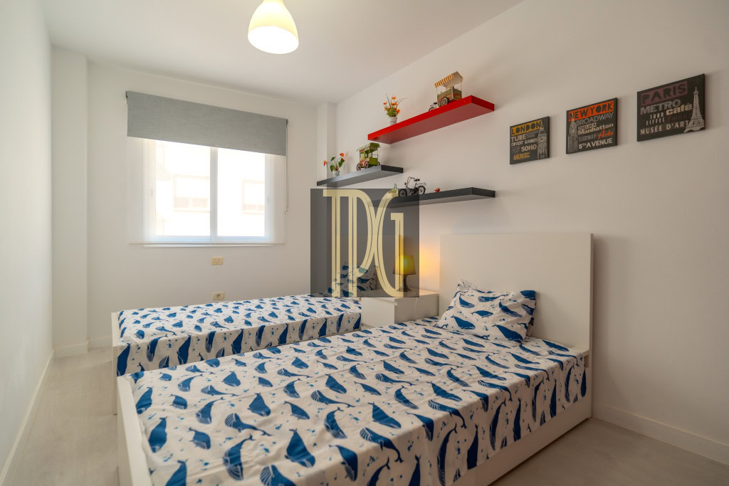Twin bedroom with two single beds, white headboards, and blue whale-pattern bedding under a window with a roller blind.