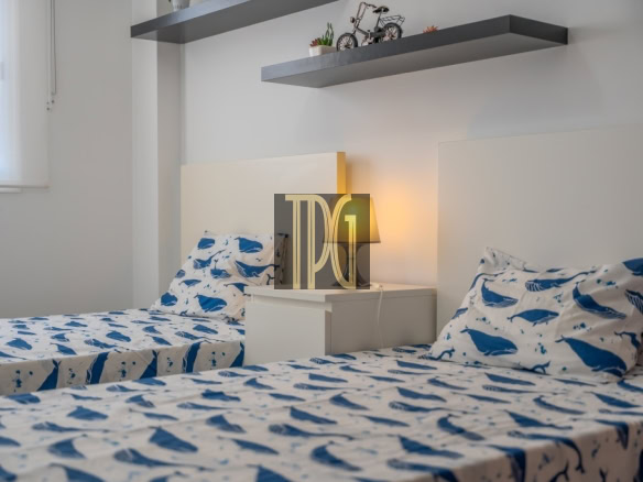 Twin bedroom with two single beds covered in blue whale-pattern bedding, a white nightstand between them, and a lit bedside lamp.