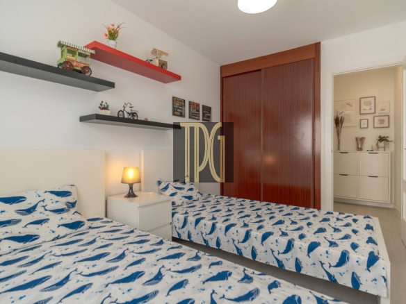 Twin bedroom with white headboards, two single beds in whale-pattern blue and white bedding, a nightstand lamp between them, and wall shelves with toys and decor.