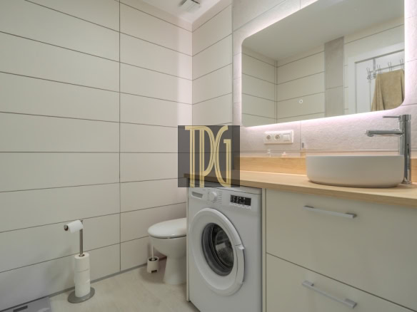 Modern bathroom with white tiled walls, wooden countertop, a vessel sink, chrome faucet, and a front-loading washing machine under the counter.