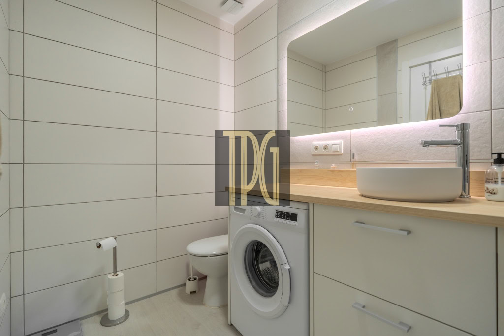 Modern bathroom with white tiled walls, wooden countertop, a vessel sink, chrome faucet, and a front-loading washing machine under the counter.