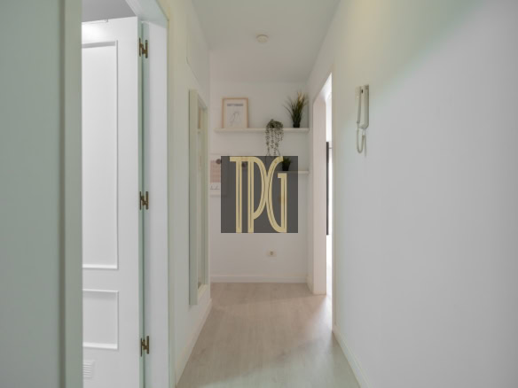 Bright, narrow hallway with pale green walls, white doors, and light wood floor, end table with plants and decor.