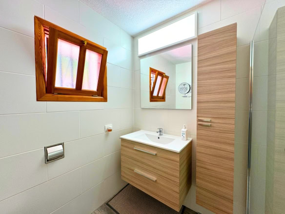 Small modern bathroom with a light wood vanity, white sink, large mirror, and a frosted angled window.