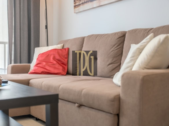 Brown fabric sofa with a red accent pillow and white cushions in a living room, with a black coffee table nearby.
