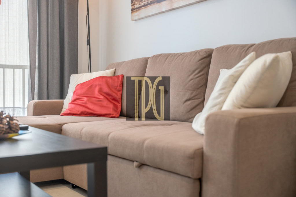 Brown fabric sofa with a red accent pillow and white cushions in a living room, with a black coffee table nearby.