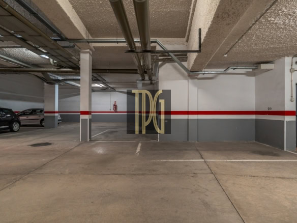Underground parking garage with concrete pillars, a red stripe along the wall, and cars parked on the left.