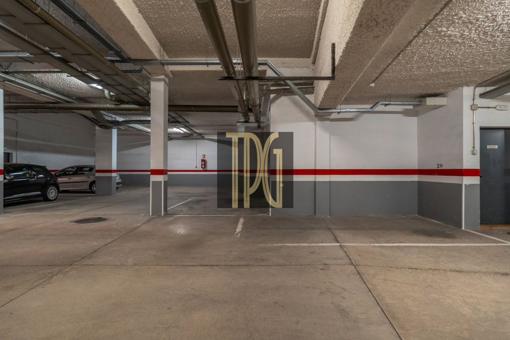 Underground parking garage with concrete pillars, a red stripe along the wall, and cars parked on the left.
