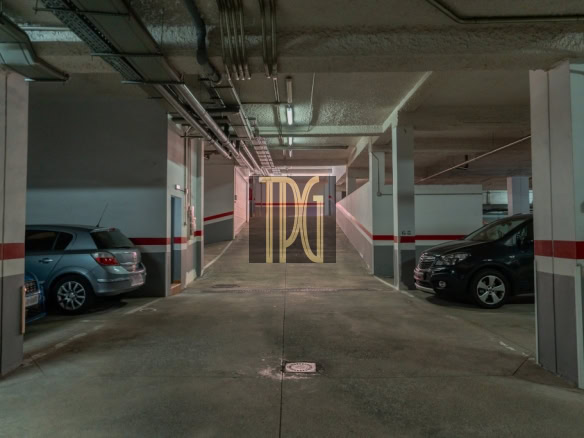 Underground parking garage aisle with cars parked on both sides and a concrete corridor ahead.