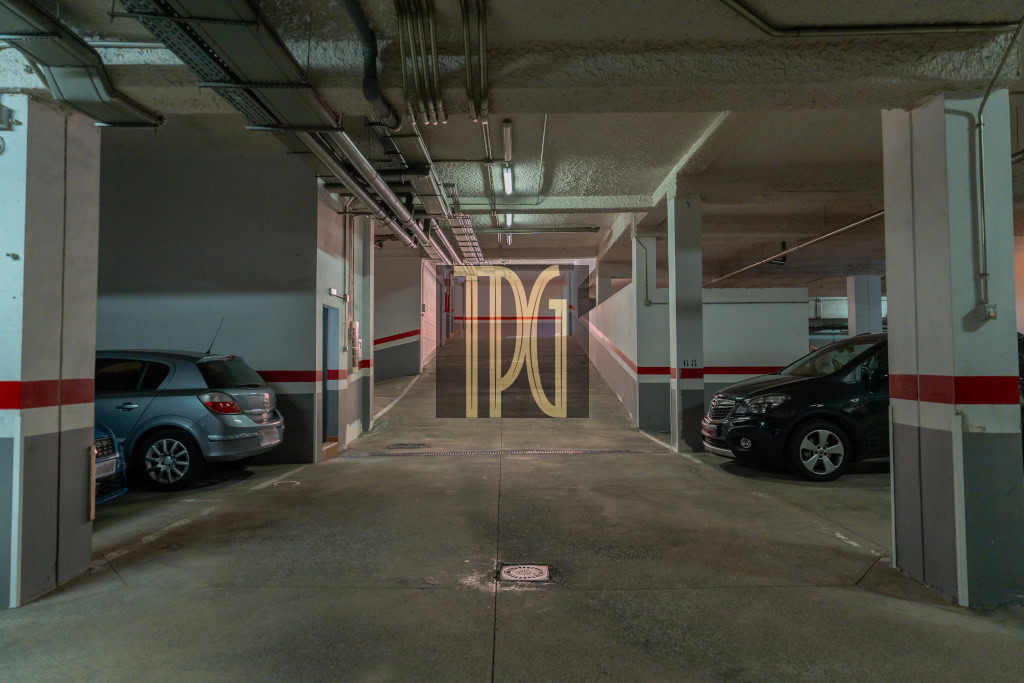 Underground parking garage aisle with cars parked on both sides and a concrete corridor ahead.