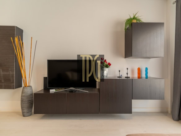 Modern living room setup featuring a dark wood media console, a flat-screen TV, and decorative items including a tall vase with sticks on the left and a plant on a wall cabinet on the right.