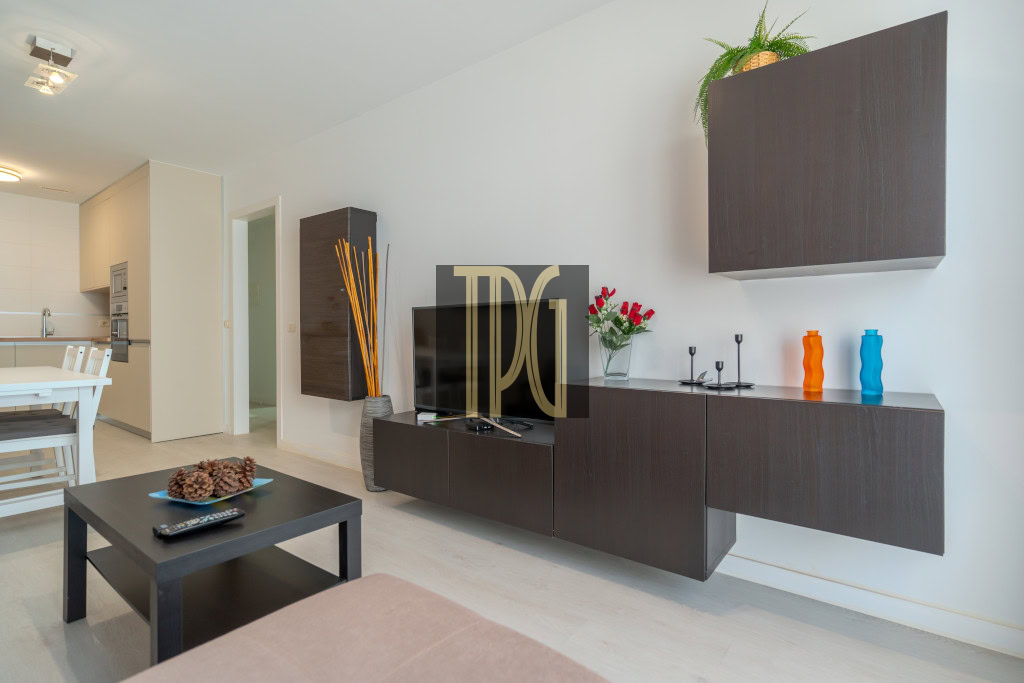 Modern living room with a dark wood wall unit, TV, and black coffee table; pinecone centerpiece and colorful vases on the sideboard.