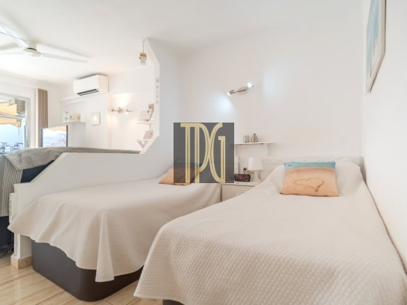 Bright hotel room with two single beds in white bedding, a window view of the city, and built-in shelves.