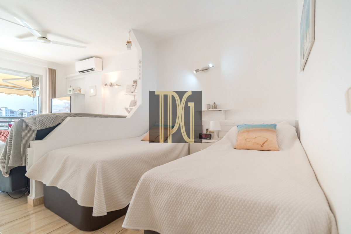 Bright hotel room with two single beds in white bedding, a window view of the city, and built-in shelves.