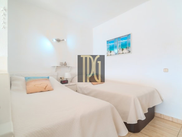 Bright hotel-style twin bedroom with two single beds in white bedding and a peach heart-decorated pillow, nightstand and beach artwork on the wall behind.