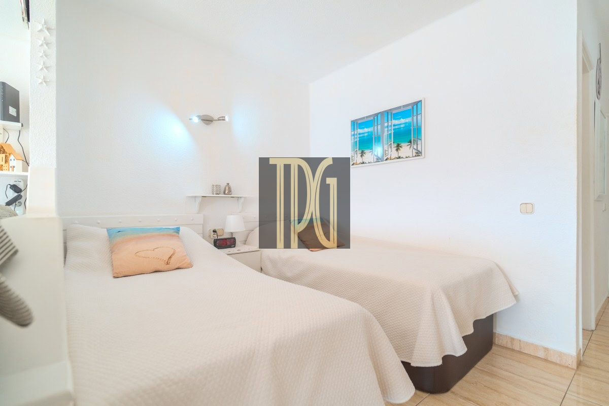 Bright hotel-style twin bedroom with two single beds in white bedding and a peach heart-decorated pillow, nightstand and beach artwork on the wall behind.