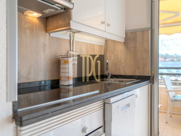 Compact kitchen with white cabinets, black countertop, paper towel holder, and a sink beside a dishwasher.