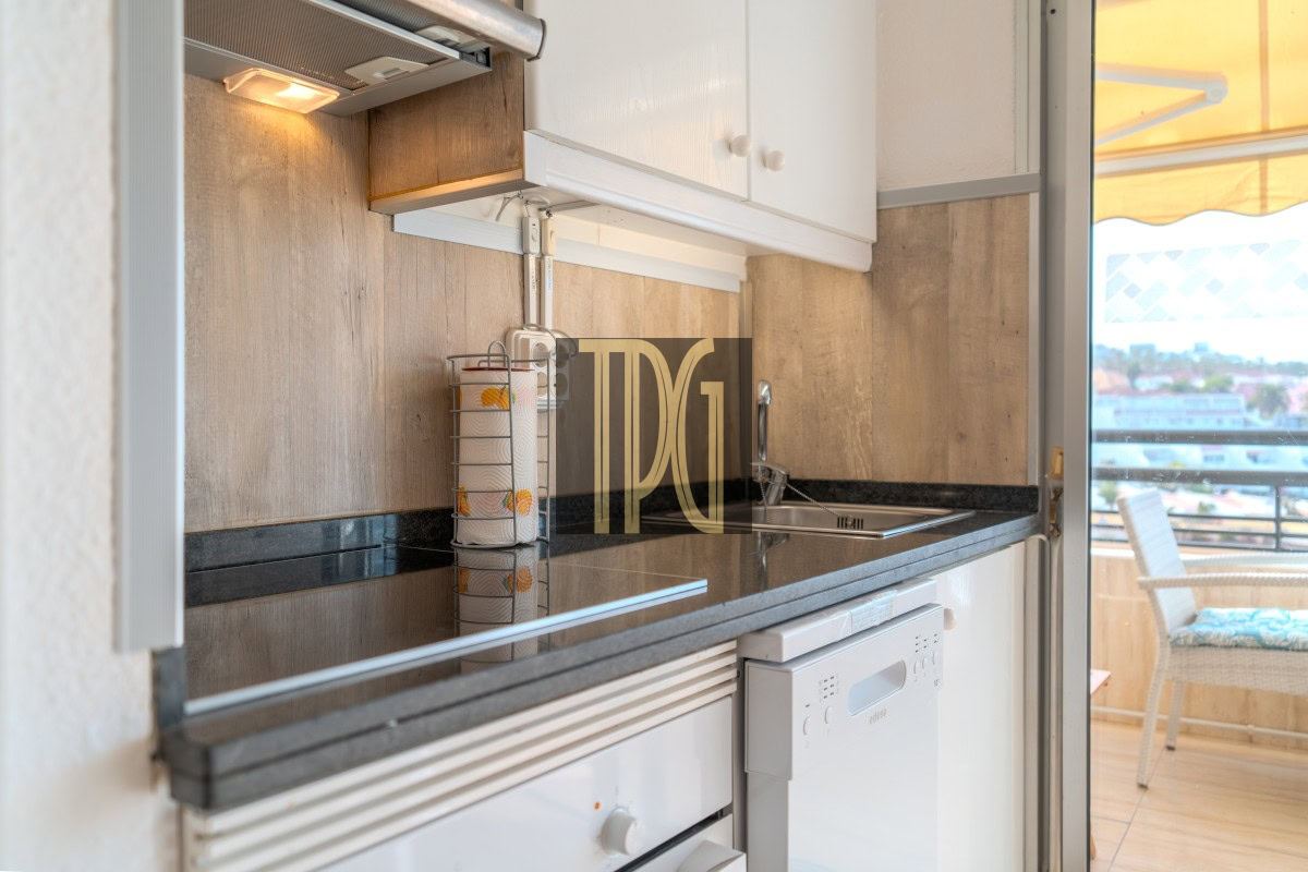Compact kitchen with white cabinets, black countertop, paper towel holder, and a sink beside a dishwasher.