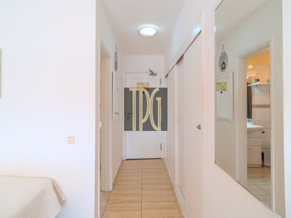 Bright, narrow hallway in a white-walled home with tiled floor, a full-length mirror on the right, and a bathroom visible through an open door on the far right side