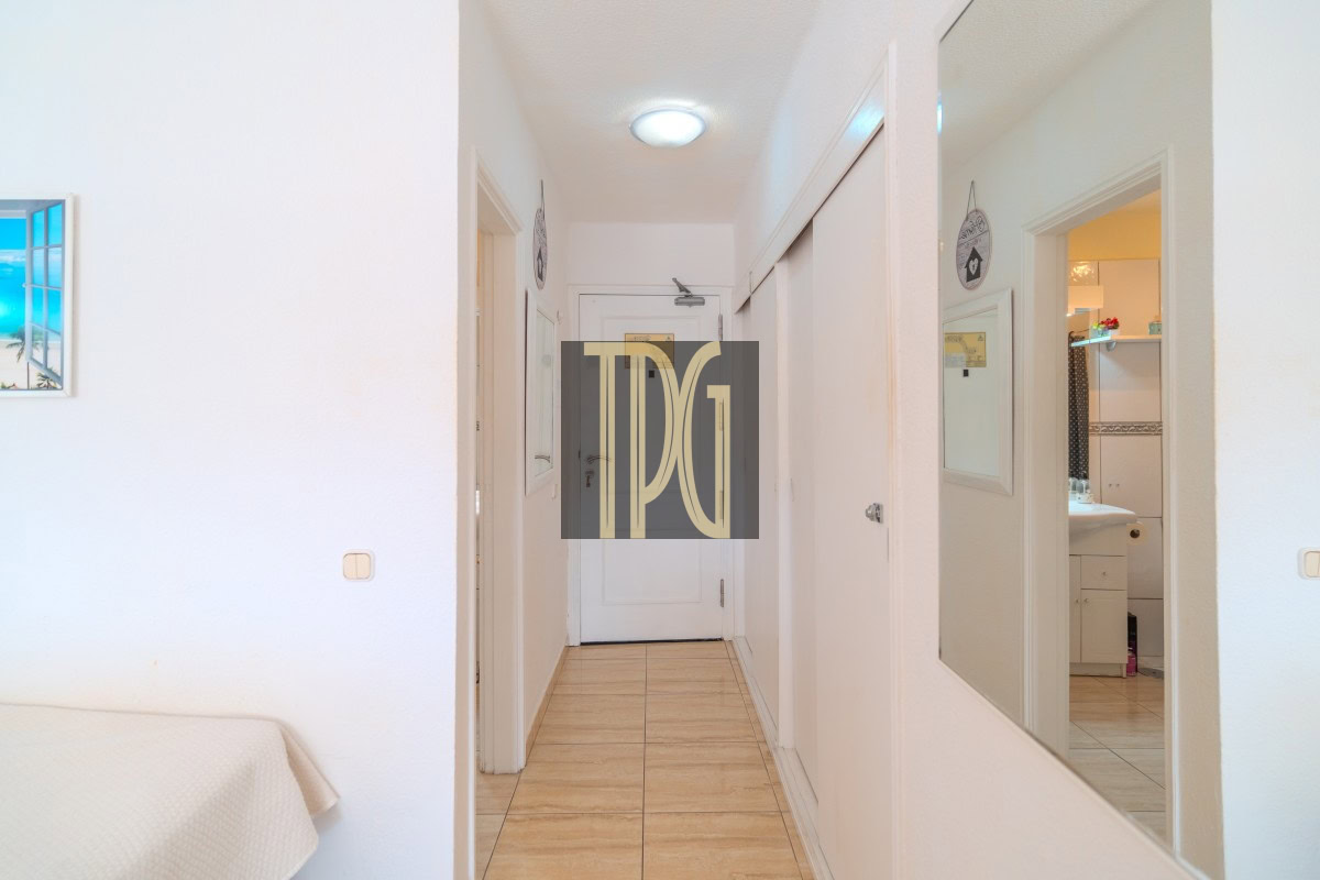 Bright, narrow hallway in a white-walled home with tiled floor, a full-length mirror on the right, and a bathroom visible through an open door on the far right side
