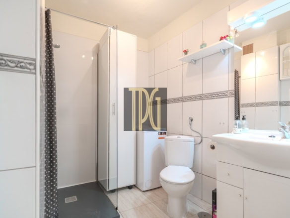 Bright white bathroom with a glass shower enclosure, toilet, washing machine, and a white sink vanity.