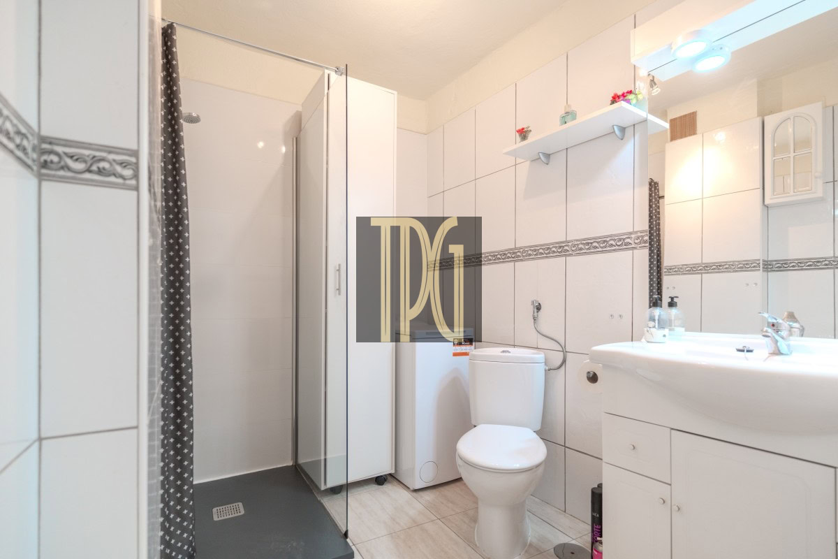 Bright white bathroom with a glass shower enclosure, toilet, washing machine, and a white sink vanity.