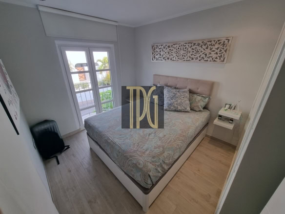 Cozy bedroom with a upholstered headboard bed, patterned bedding, and a decorative wall panel above; door to a balcony on the left.