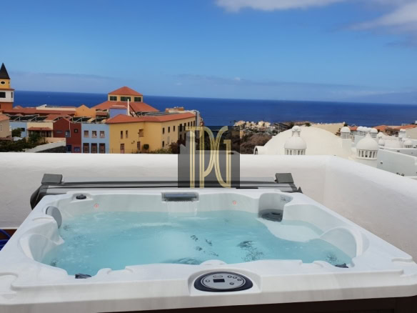 Hot tub on a balcony with a view of colorful coastal buildings and the blue ocean beyond.