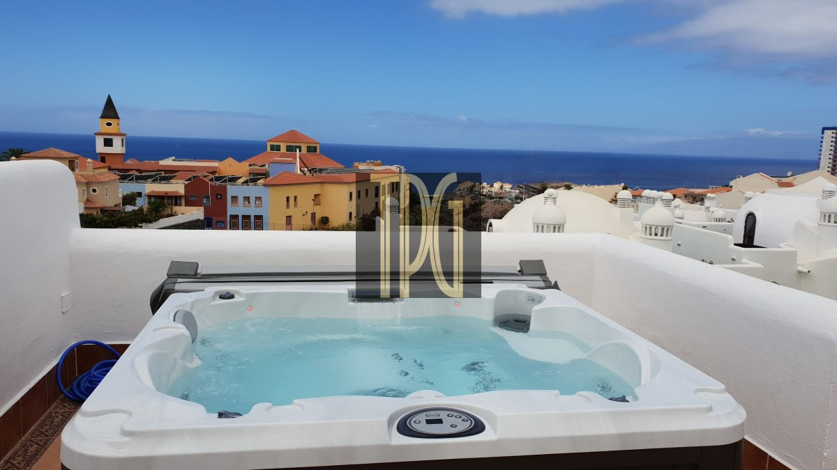 Hot tub on a balcony with a view of colorful coastal buildings and the blue ocean beyond.