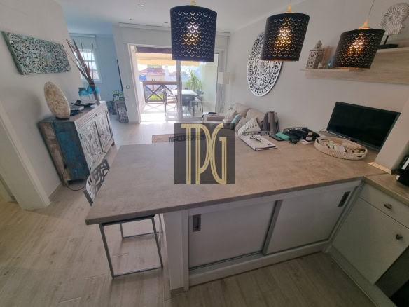 Open-concept kitchen with a large gray island, pendant lights, and a living area with a sofa and balcony door beyond.