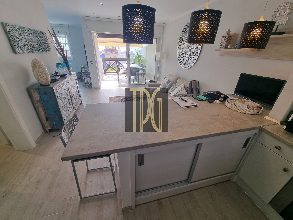 Open-concept kitchen with a large gray island, pendant lights, and a living area with a sofa and balcony door beyond.