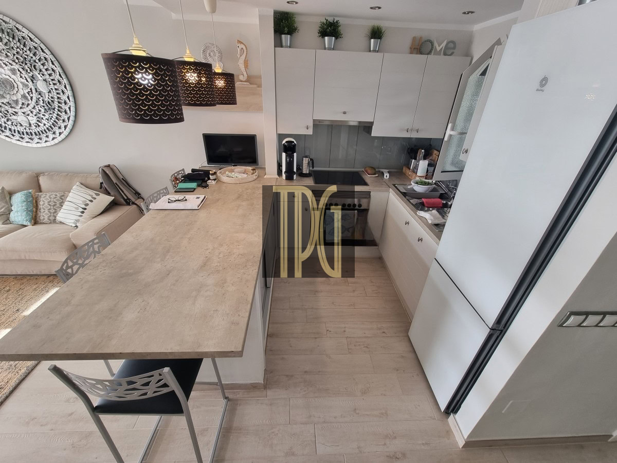 Open-concept kitchen with a long beige island, white cabinets, stainless appliances, and a living room sofa visible nearby.