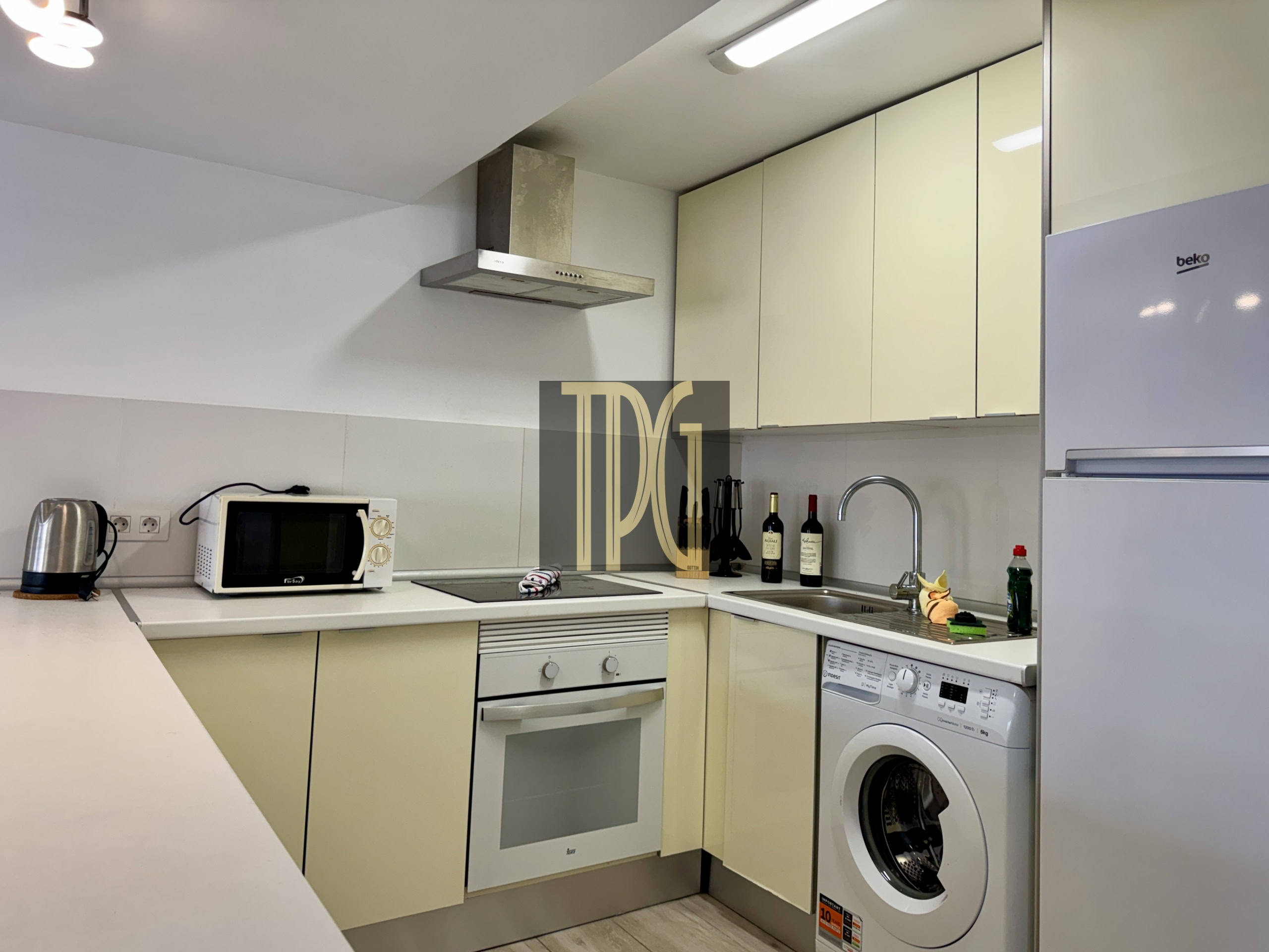 Modern kitchen with cream cabinets, stainless steel range hood, microwave, oven, and washing machine along a counter line.