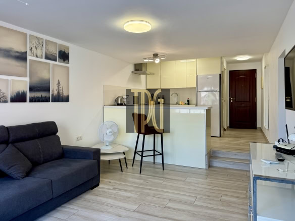 Open-plan living area with a dark blue sofa, wall art, and a white kitchen island with bar-height chairs.