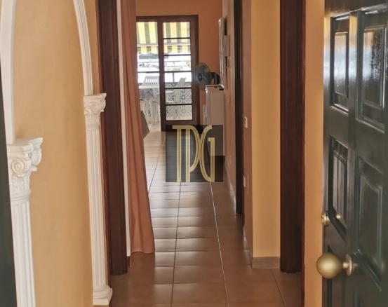Bright hallway with beige walls, white decorative arch on the left, brown doors along the corridor, and a sunlit room at the far end.