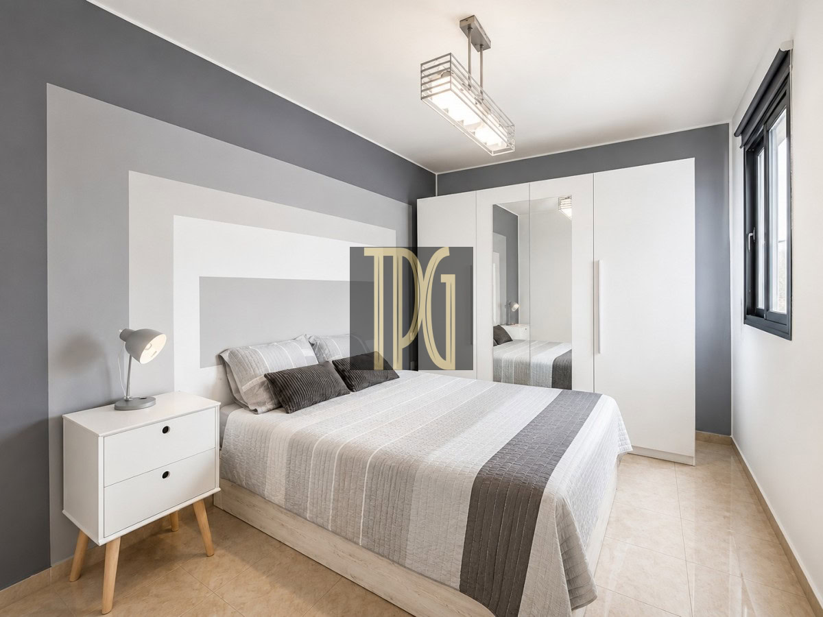 Unknown-11 Modern bedroom with a gray geometric accent wall, a white bed, and a large white wardrobe with mirrored doors.