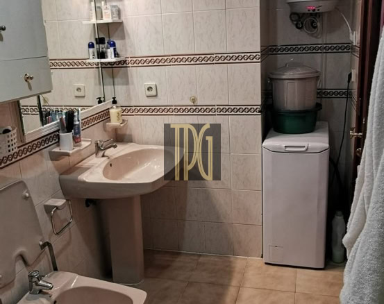 Small beige-tiled bathroom with toilet, bidet, pedestal sink, mirror cabinet, and a washing machine under a wall-mounted water heater.