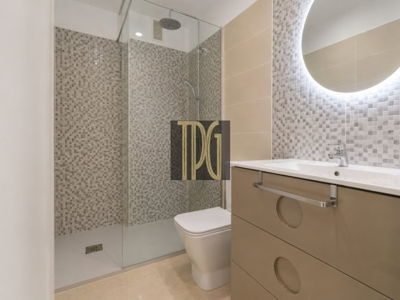 Modern bathroom with glass shower enclosure, mosaic tile walls, and a beige vanity with circular drawer cutouts beside a backlit round mirror.