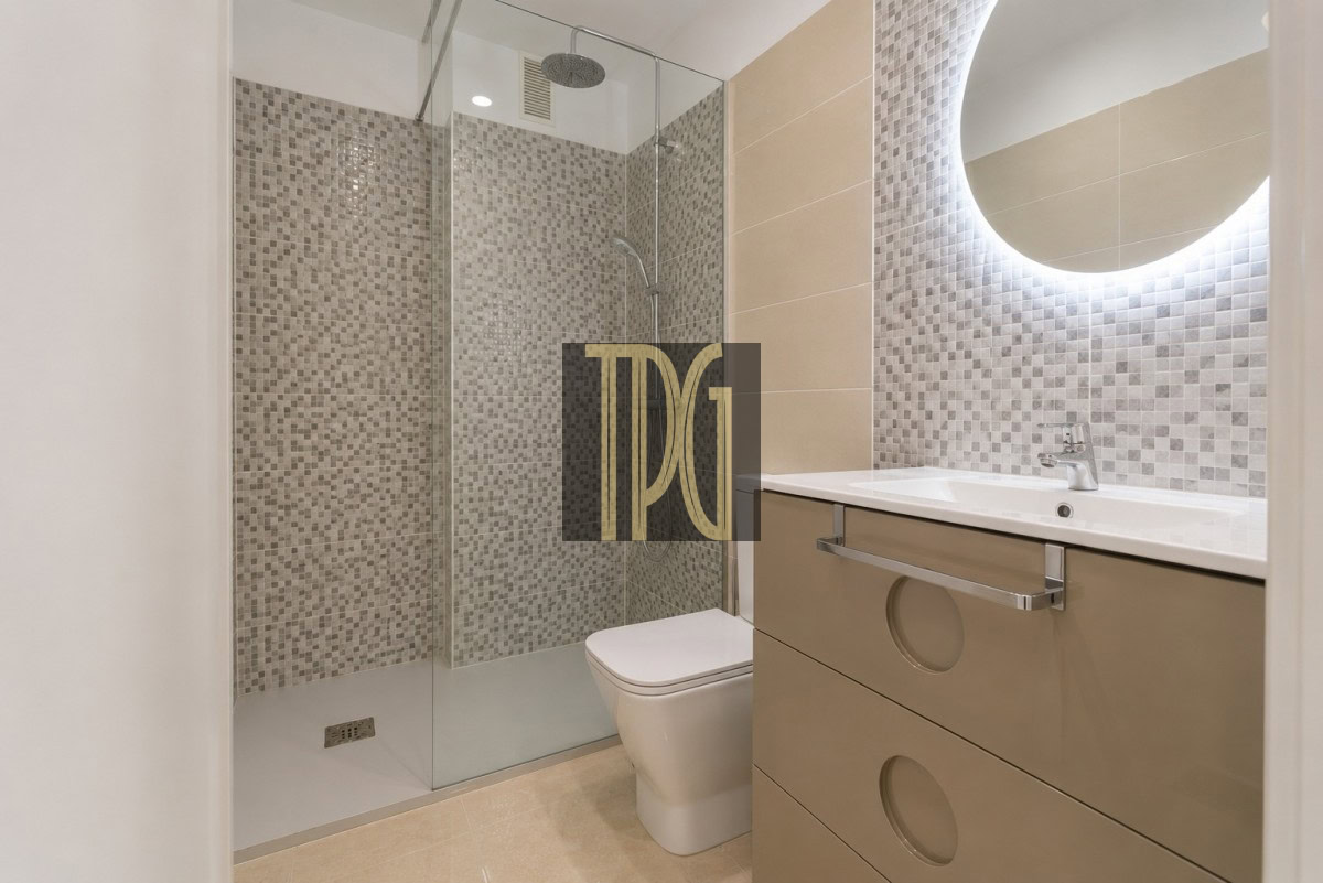 Unknown-2 Modern bathroom with glass shower enclosure, mosaic tile walls, and a beige vanity with circular drawer cutouts beside a backlit round mirror.
