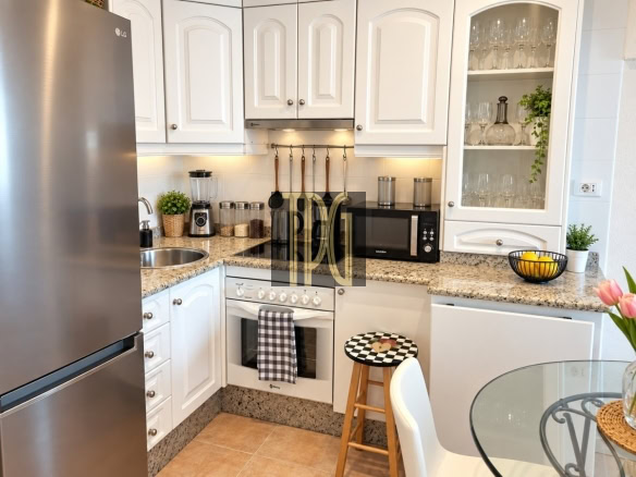 Modern L-shaped kitchen with white cabinets, stainless steel fridge, gas stove, and microwave on a granite countertop.