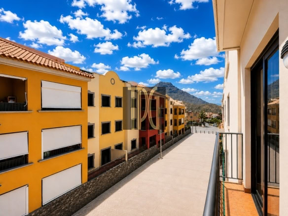 Balcony view over a colorful residential row of yellow and orange buildings, with a tiled promenade and distant mountains under a blue sky.
