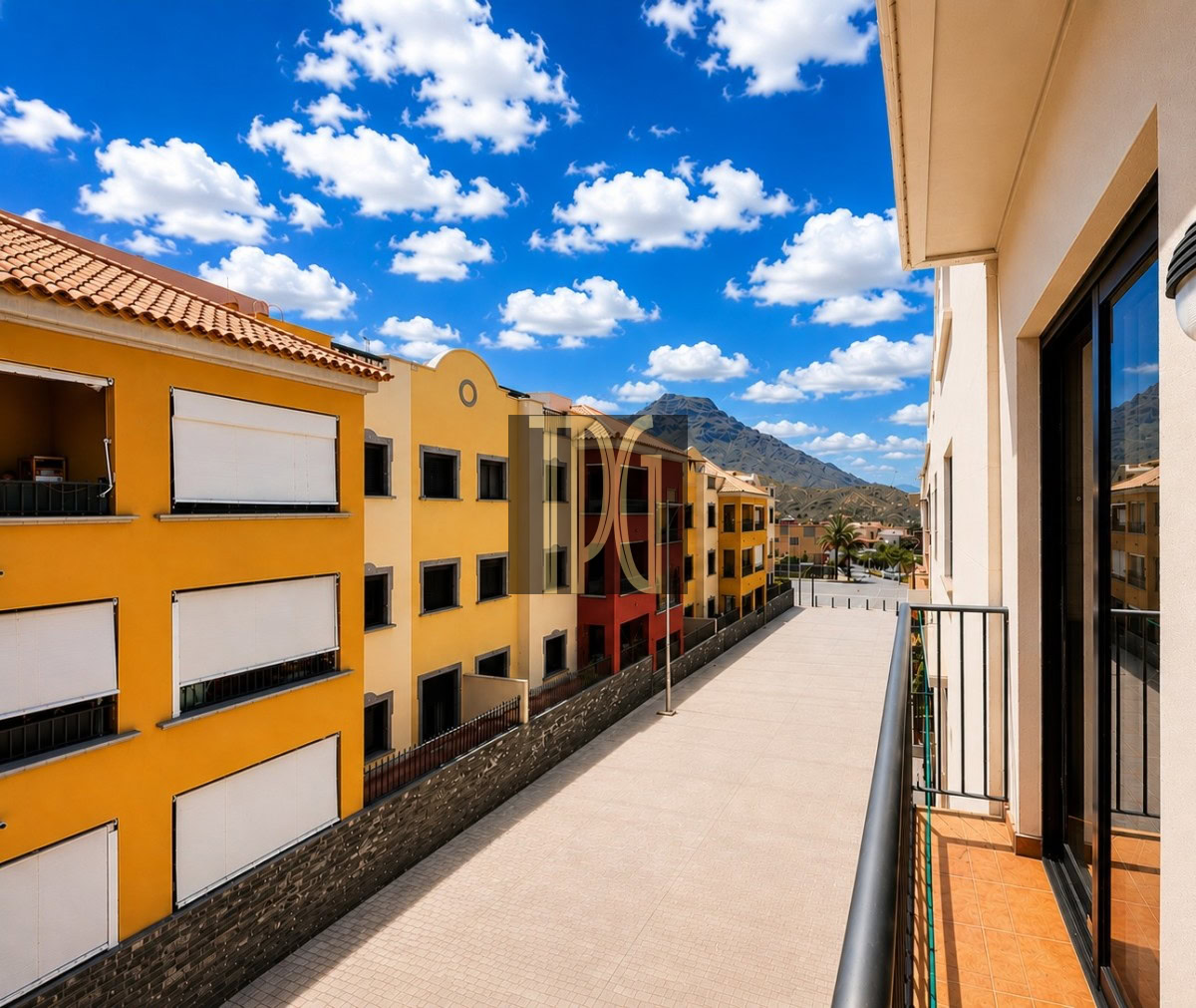Unknown-5 Balcony view over a colorful residential row of yellow and orange buildings, with a tiled promenade and distant mountains under a blue sky.