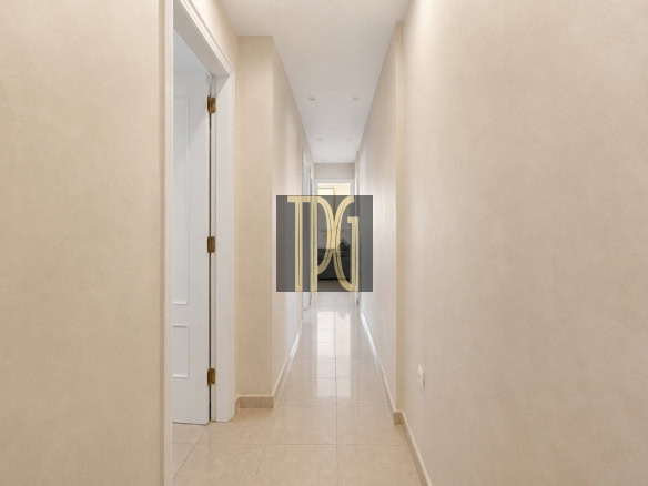 Long beige hallway with tiled floor and white doors, leading to a bright end.