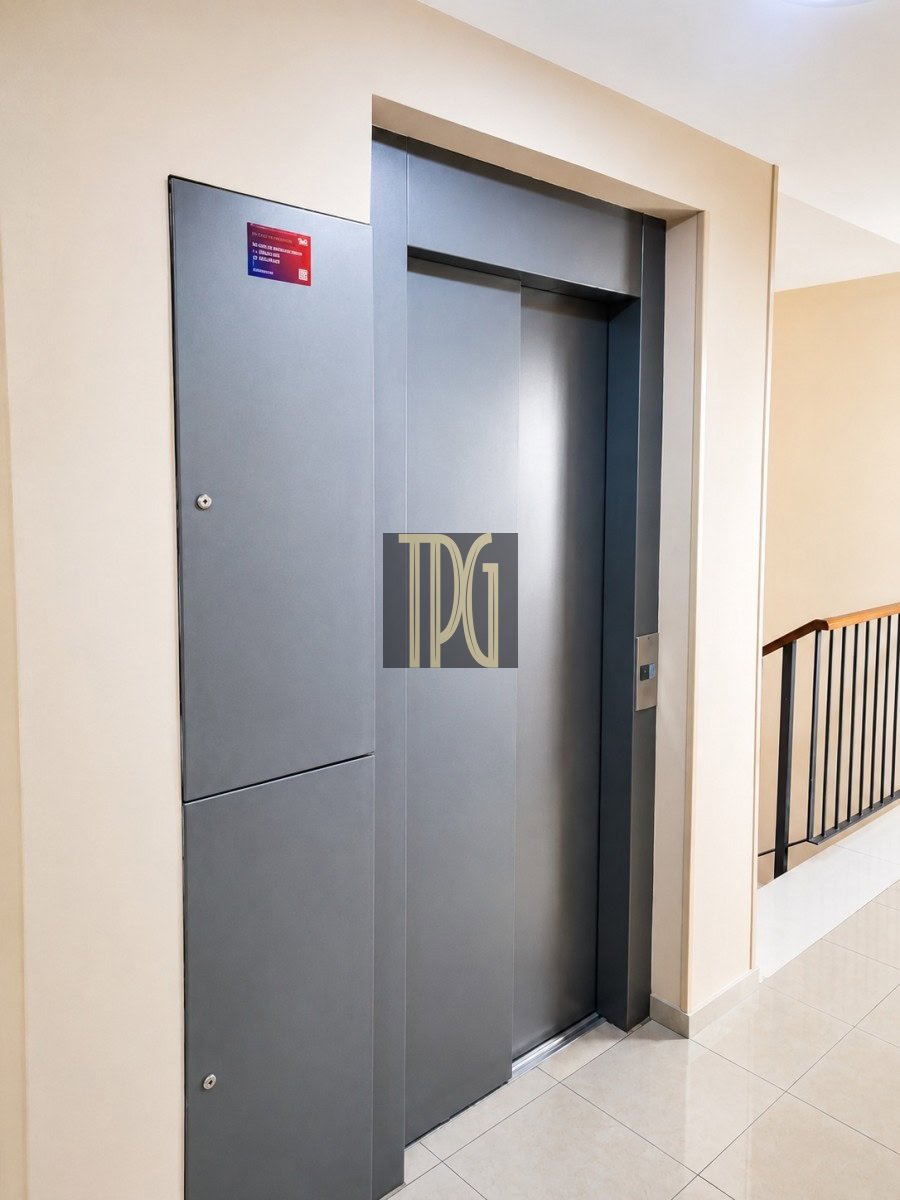 Unknown-6 Grey elevator doors closed in a beige-halled corridor, with a railing on the right side and tiled floor.