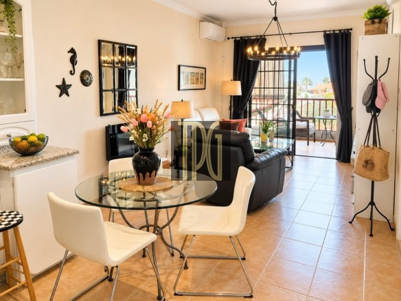 Open-concept living room and dining area with a glass round table, white chairs, and a black sofa leading to a balcony.