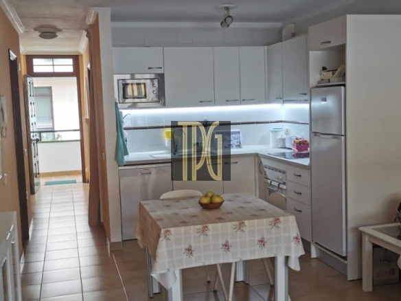 Cozy kitchen with white cabinets, fridge and microwave, and a small table with a floral tablecloth in peach-colored walls.