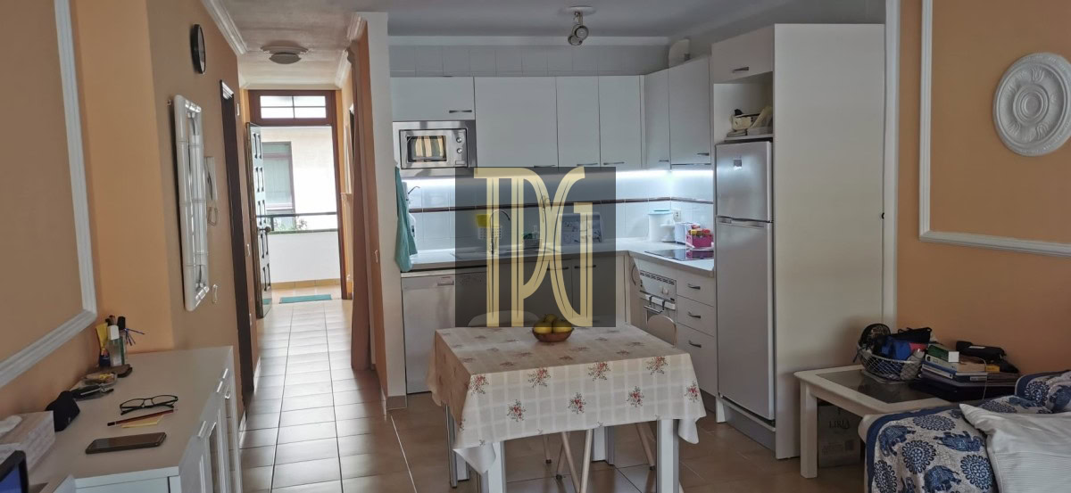 Cozy kitchen with white cabinets, fridge and microwave, and a small table with a floral tablecloth in peach-colored walls.