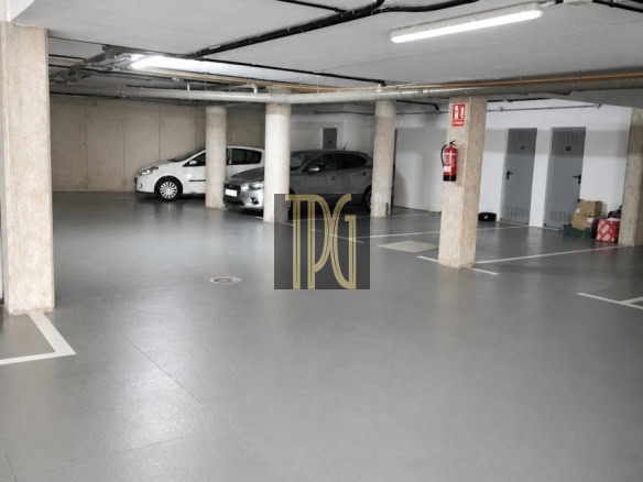 Underground parking garage with concrete pillars, two parked cars, exposed pipes, and a fire extinguisher on a column.