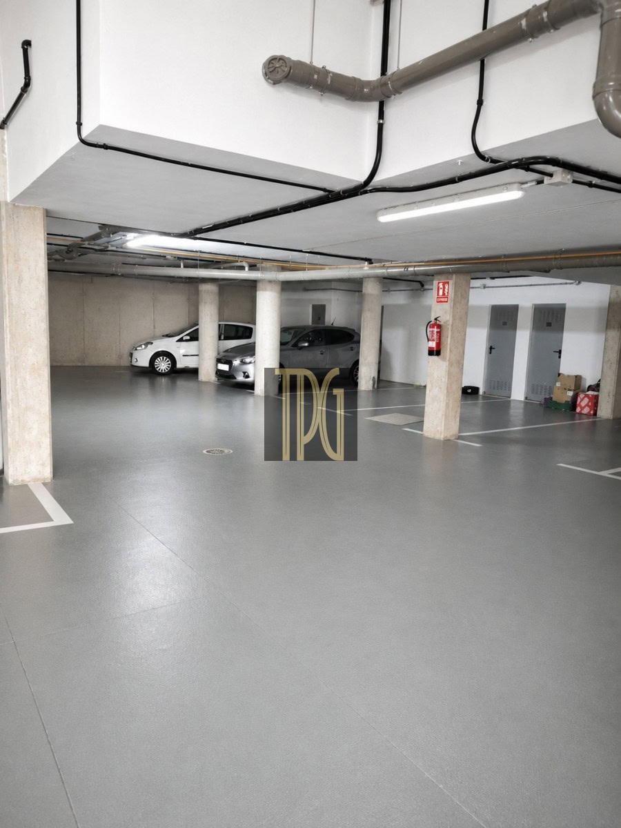 Unknown-7 Underground parking garage with concrete pillars, two parked cars, exposed pipes, and a fire extinguisher on a column.